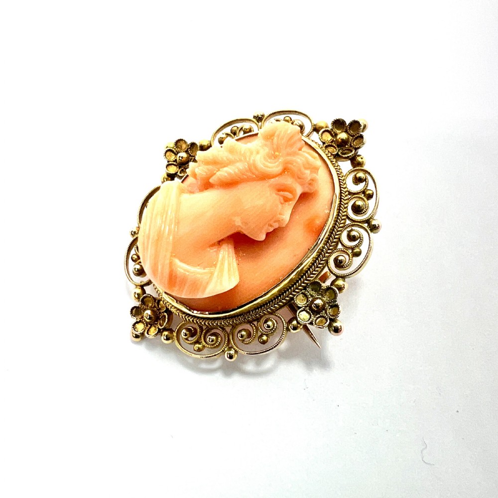 An oval Victorian brooch featuring a hand-carved peach coral classical female cameo profile set within a gold filigree wirework frame. View II