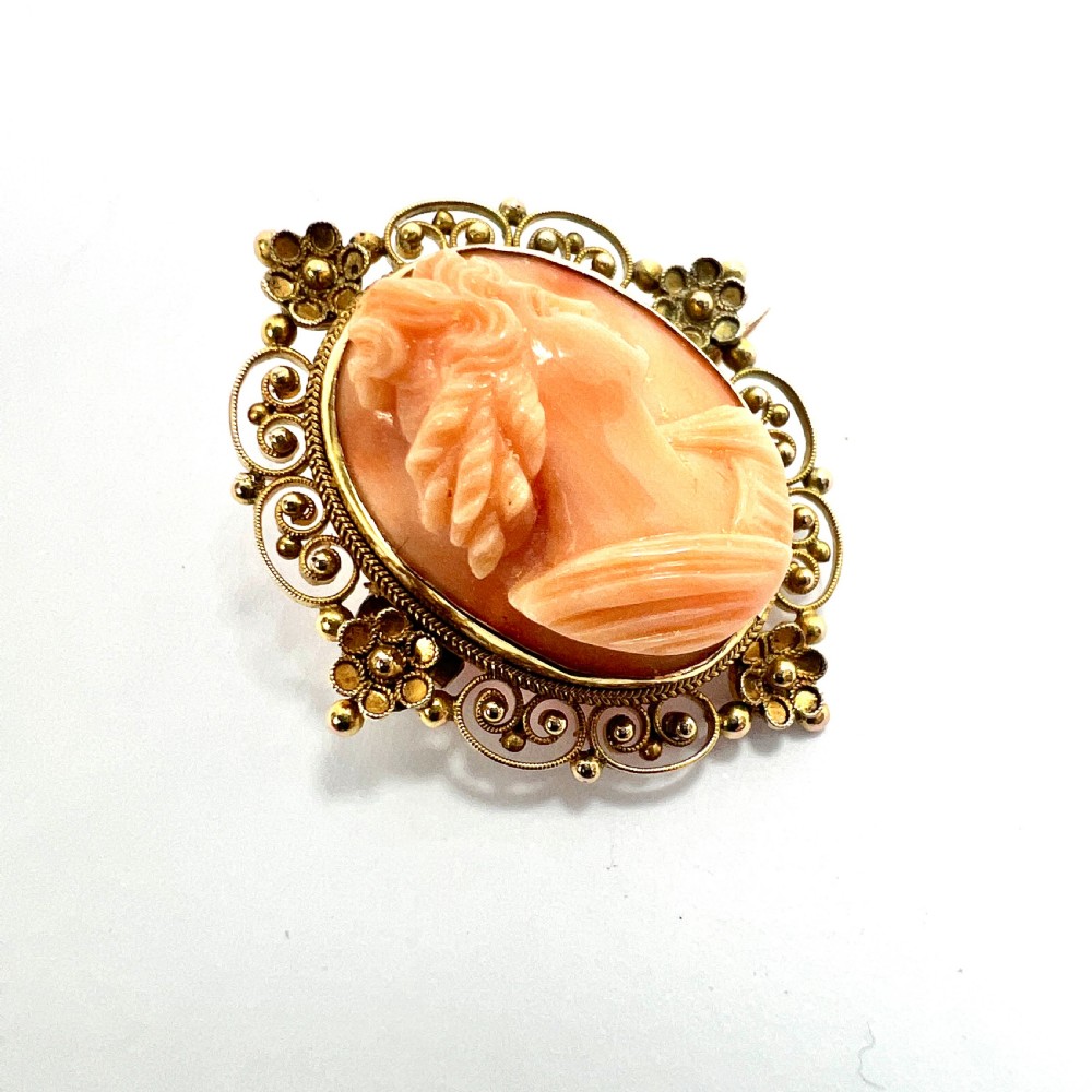 An oval Victorian brooch featuring a hand-carved peach coral classical female cameo profile set within a gold filigree wirework frame. View III