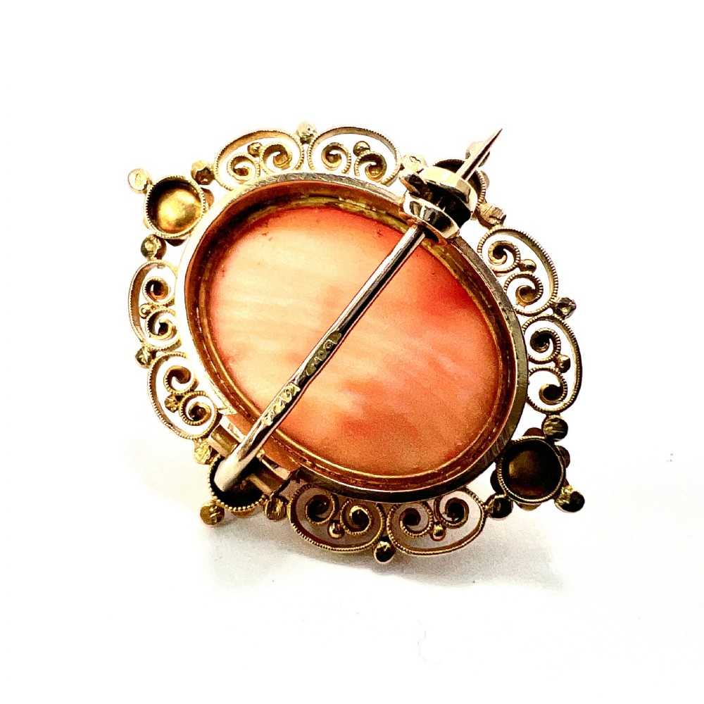 An oval Victorian brooch featuring a hand-carved peach coral classical female cameo profile set within a gold filigree wirework frame. View IV