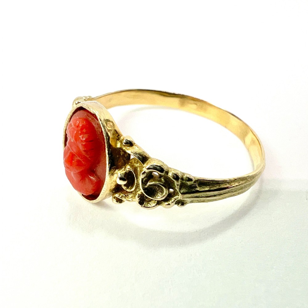 An antique gold ring featuring a central oval carved red coral cameo depicting a classical profile with decorative scrollwork shoulders. View IV