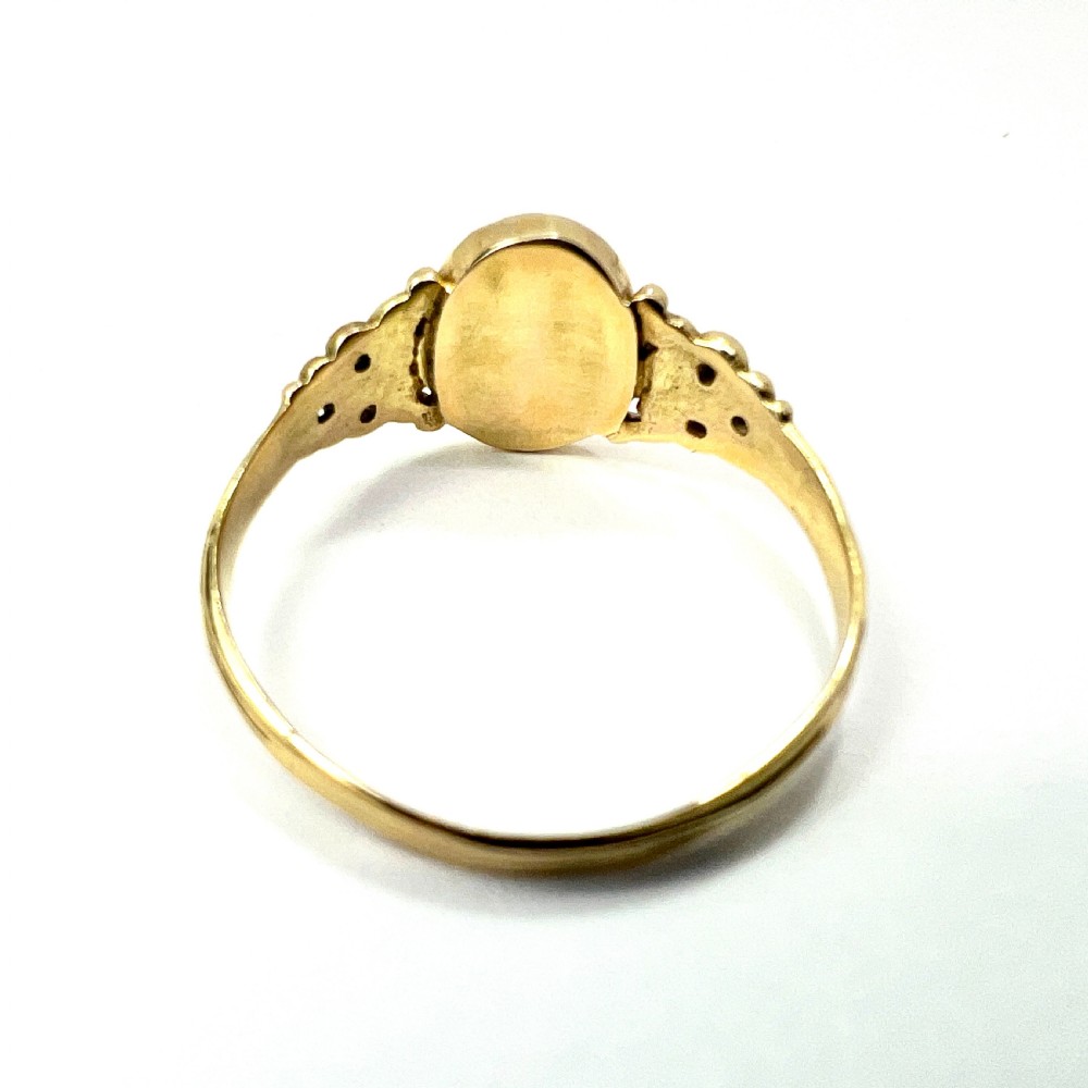 An antique gold ring featuring a central oval carved red coral cameo depicting a classical profile with decorative scrollwork shoulders. View V