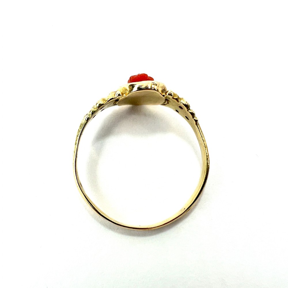 An antique gold ring featuring a central oval carved red coral cameo depicting a classical profile with decorative scrollwork shoulders. View VII