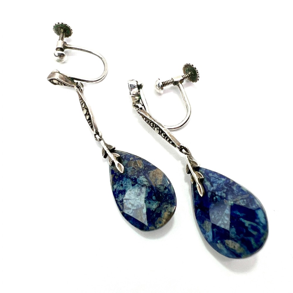 A pair of Art Deco silver screwback drop earrings featuring faceted blue teardrop stones suspended from linear marcasite-set bars.