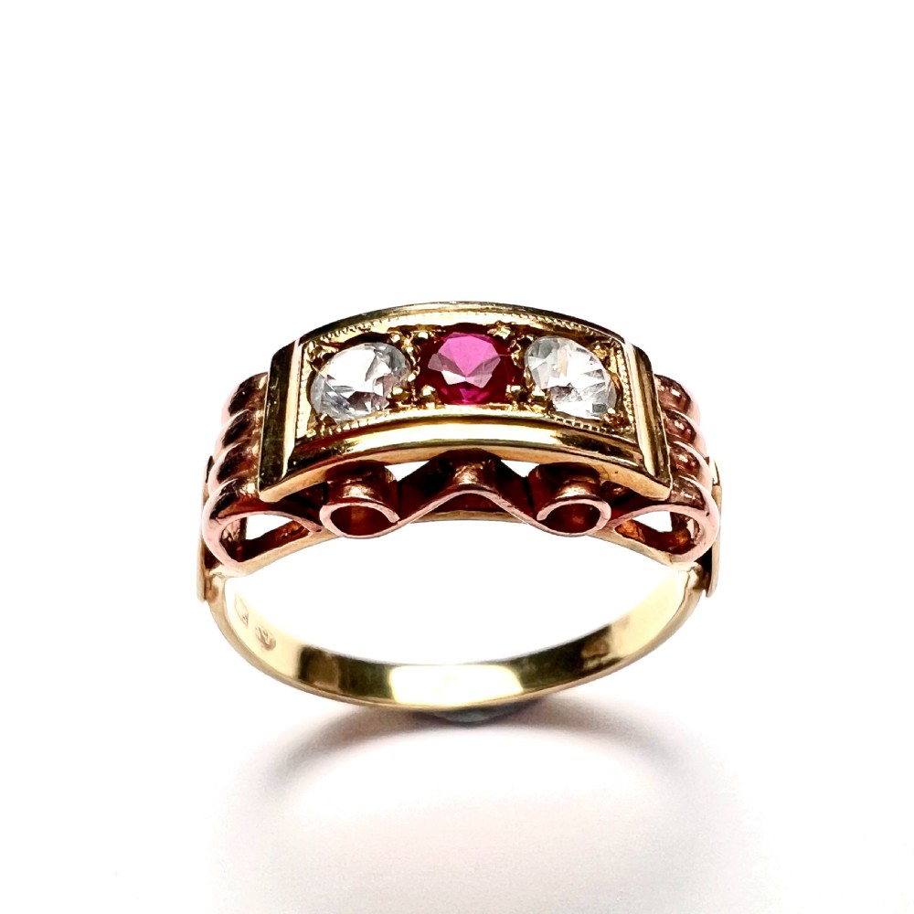 A vintage 14ct yellow and rose gold ring featuring a central red ruby paste stone flanked by two clear stones in a rectangular box setting with scrollwork shoulders.