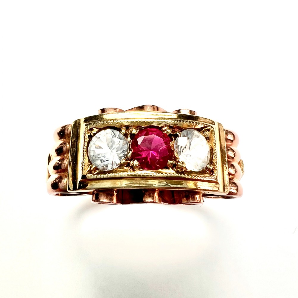 A vintage 14ct yellow and rose gold ring featuring a central red ruby paste stone flanked by two clear stones in a rectangular box setting with scrollwork shoulders. View II