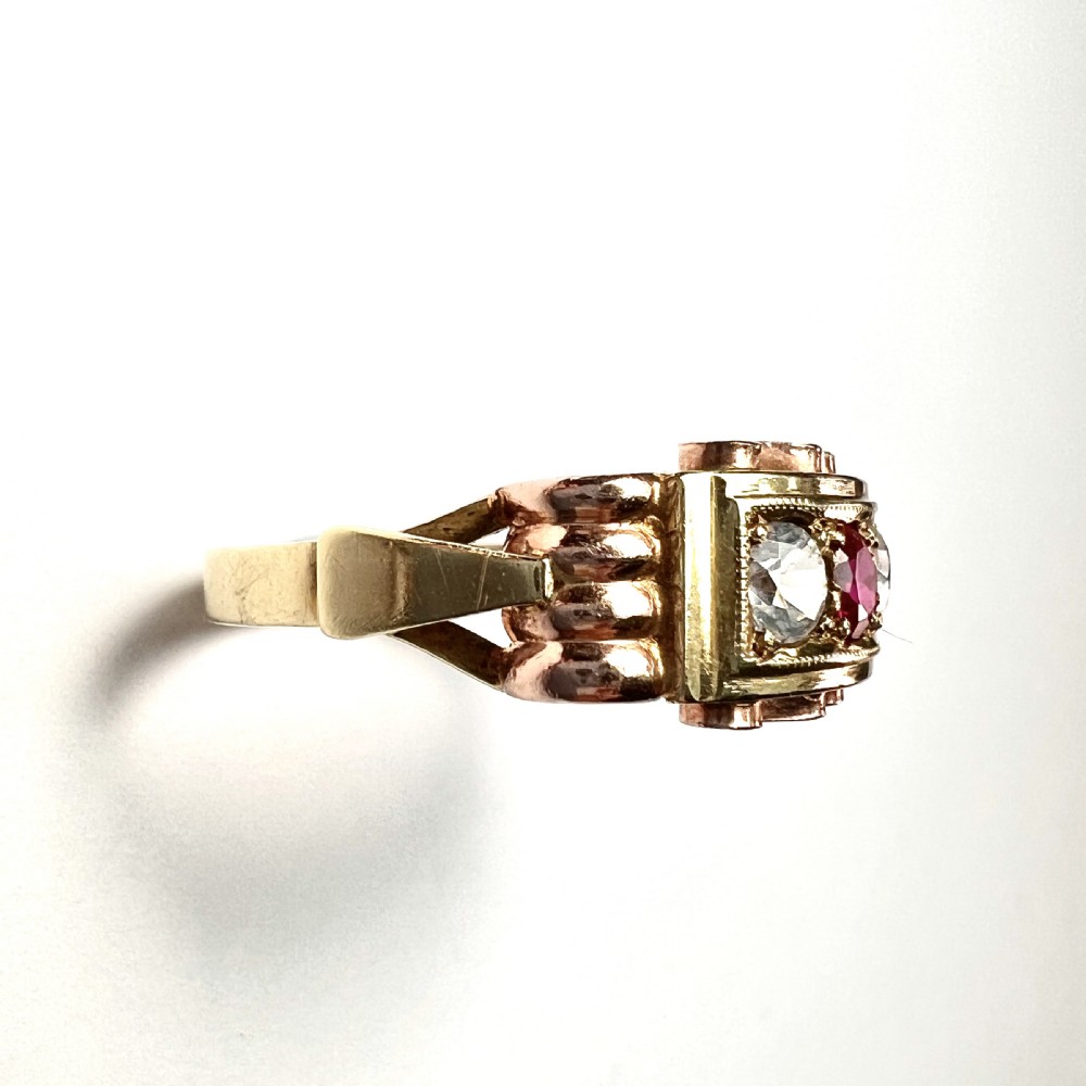 A vintage 14ct yellow and rose gold ring featuring a central red ruby paste stone flanked by two clear stones in a rectangular box setting with scrollwork shoulders. View VII