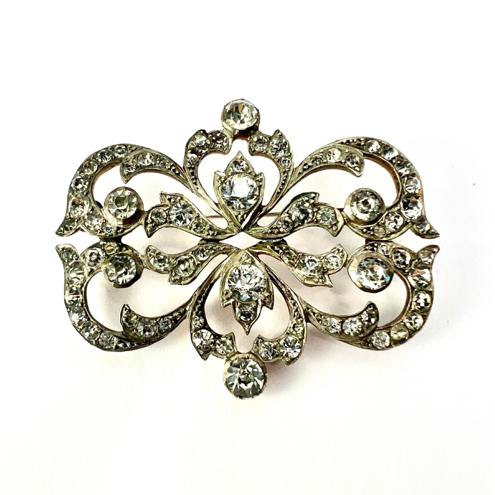 A symmetrical Victorian openwork silver brooch set with numerous faceted clear paste stones in an intricate scrolling foliate design.