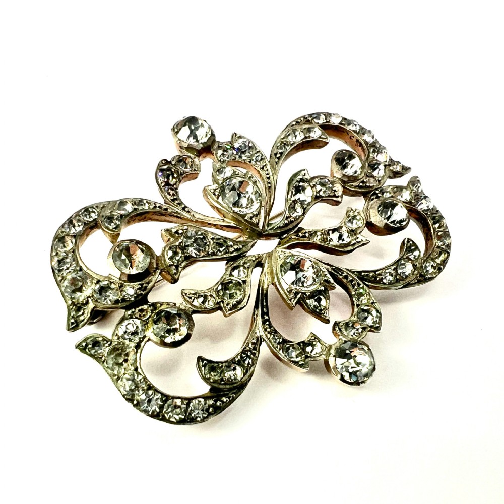 A symmetrical Victorian openwork silver brooch set with numerous faceted clear paste stones in an intricate scrolling foliate design. View III