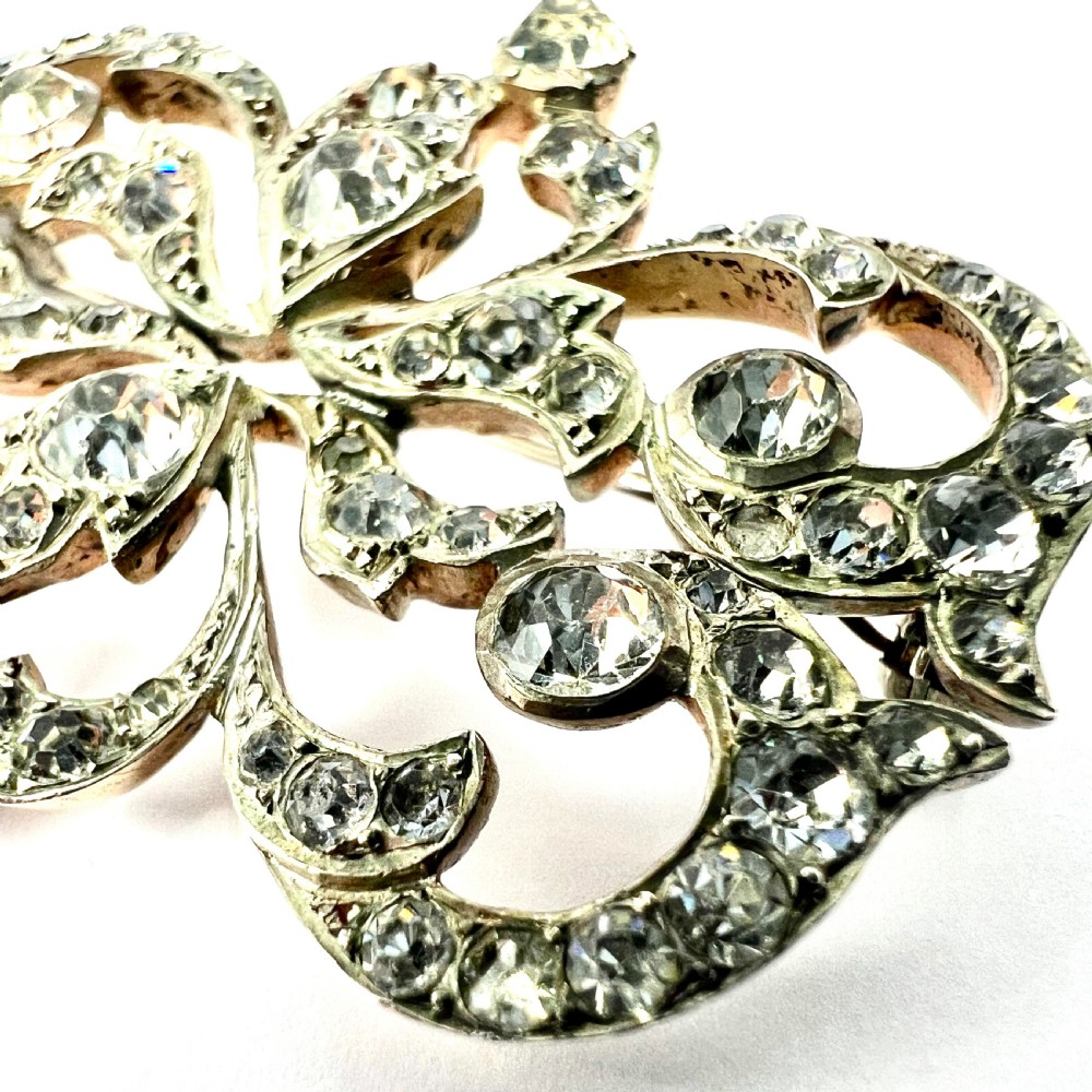 A symmetrical Victorian openwork silver brooch set with numerous faceted clear paste stones in an intricate scrolling foliate design. View V