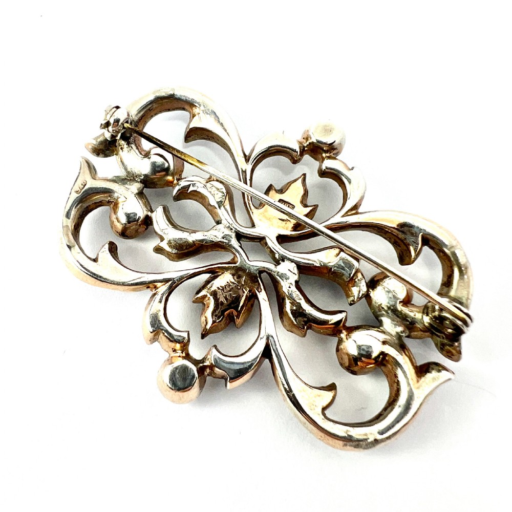 A symmetrical Victorian openwork silver brooch set with numerous faceted clear paste stones in an intricate scrolling foliate design. View VI
