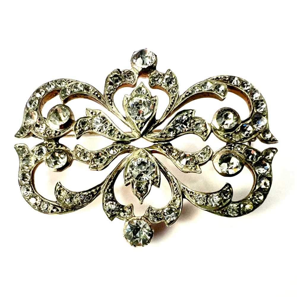 A symmetrical Victorian openwork silver brooch set with numerous faceted clear paste stones in an intricate scrolling foliate design. View VIII