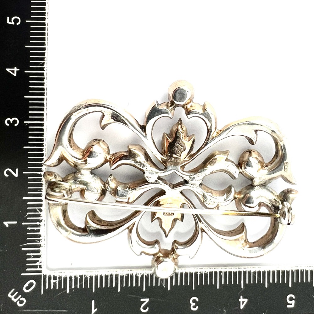 A symmetrical Victorian openwork silver brooch set with numerous faceted clear paste stones in an intricate scrolling foliate design. View IX