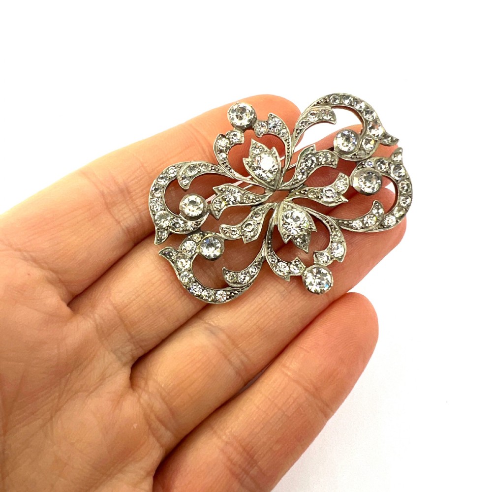 A symmetrical Victorian openwork silver brooch set with numerous faceted clear paste stones in an intricate scrolling foliate design. View X