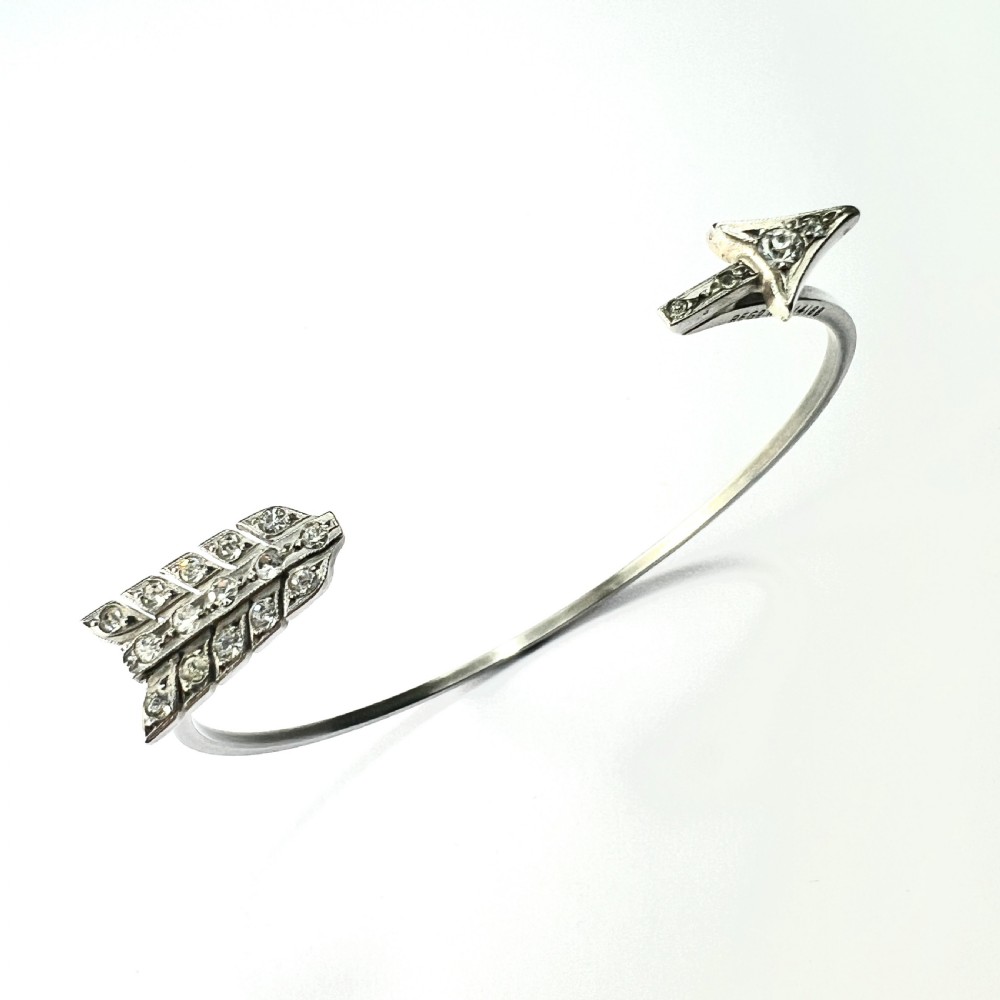 An open silver-toned metal cuff bangle designed in the shape of an arrow set with clear paste glass stones along the head and tail.