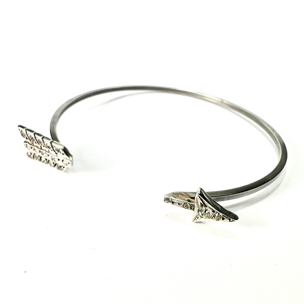 An open silver-toned metal cuff bangle designed in the shape of an arrow set with clear paste glass stones along the head and tail. View II