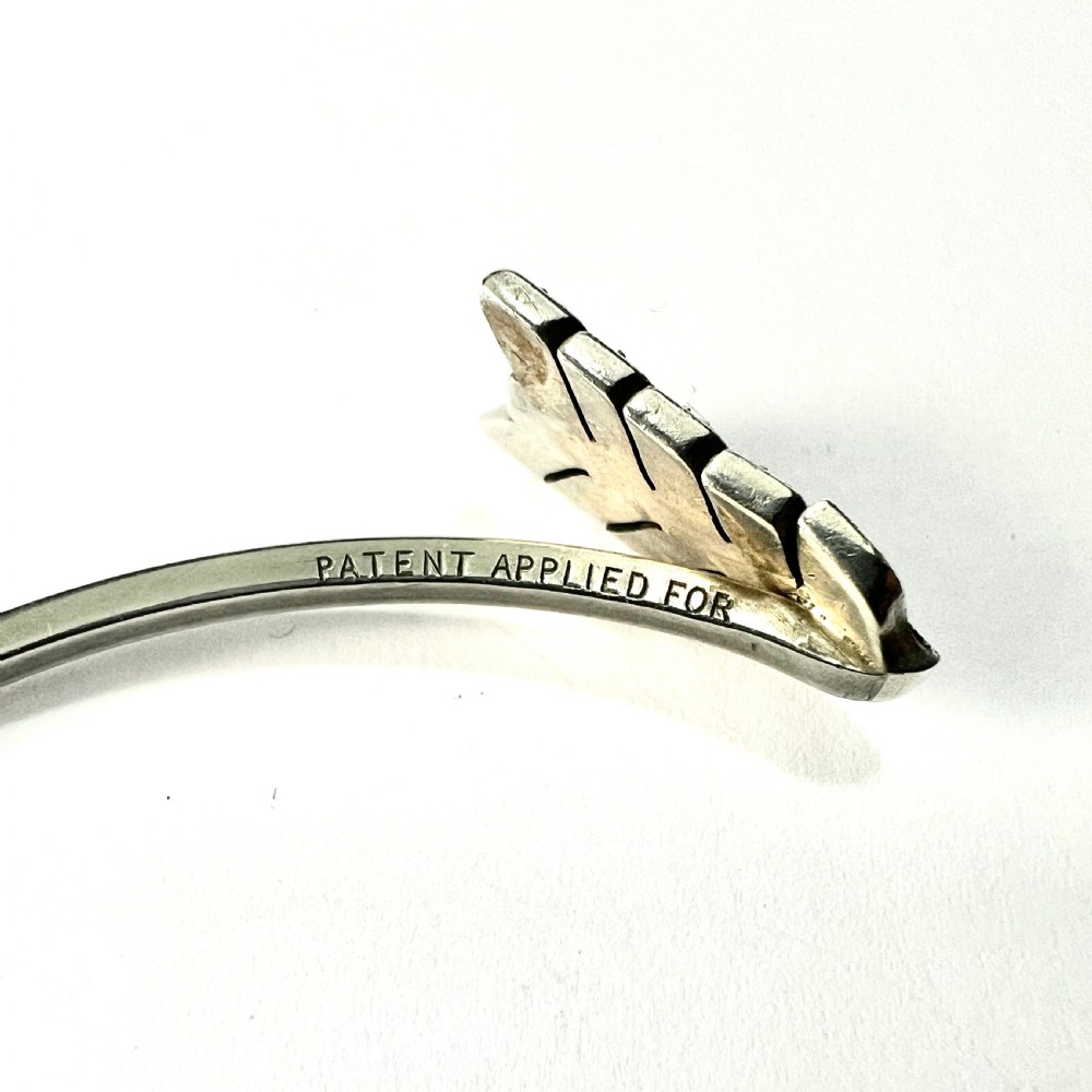 An open silver-toned metal cuff bangle designed in the shape of an arrow set with clear paste glass stones along the head and tail. View V