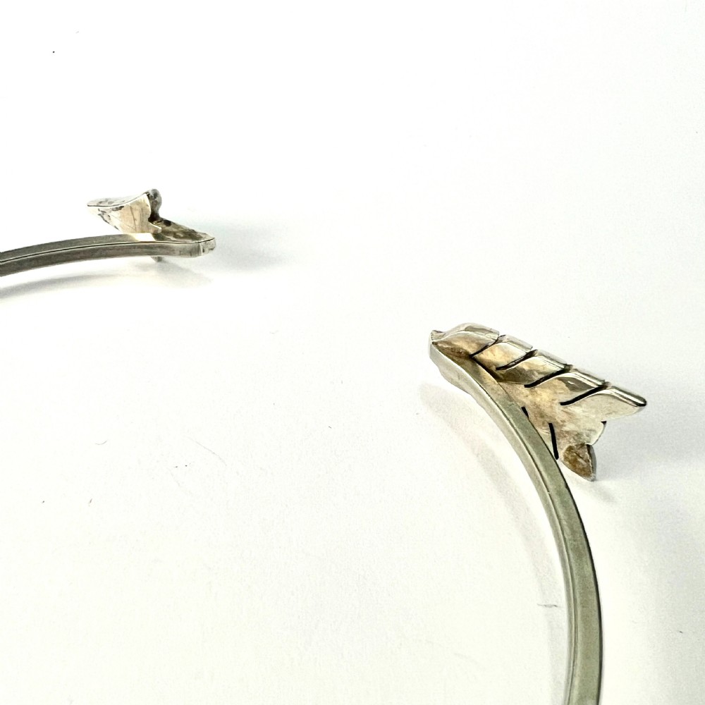 An open silver-toned metal cuff bangle designed in the shape of an arrow set with clear paste glass stones along the head and tail. View VI