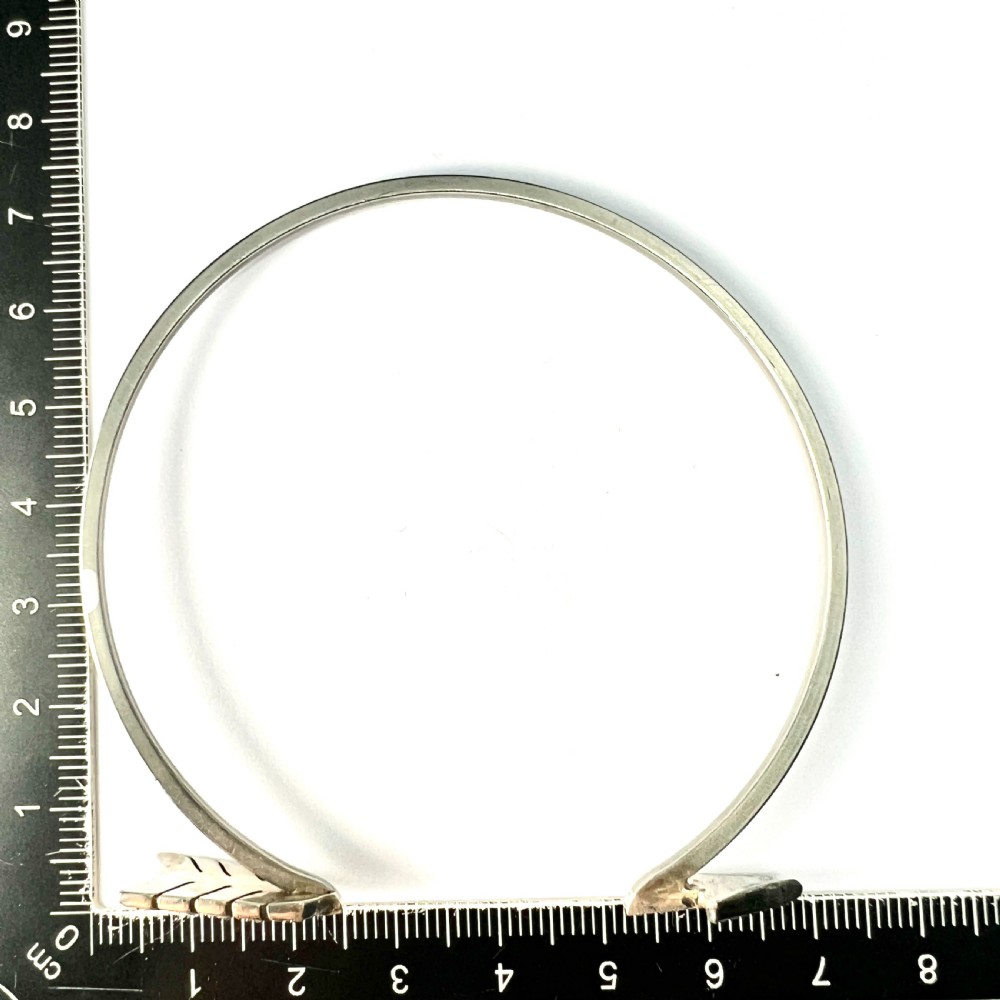 An open silver-toned metal cuff bangle designed in the shape of an arrow set with clear paste glass stones along the head and tail. View VII