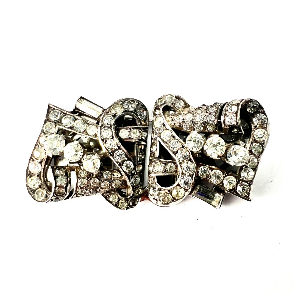An Art Deco silver-tone paste duette brooch featuring geometric scrollwork set with round and baguette cut clear paste stones.