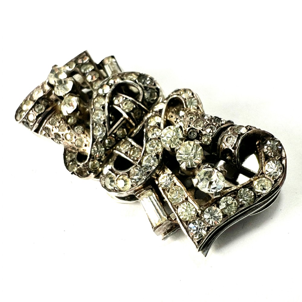 An Art Deco silver-tone paste duette brooch featuring geometric scrollwork set with round and baguette cut clear paste stones. View IV