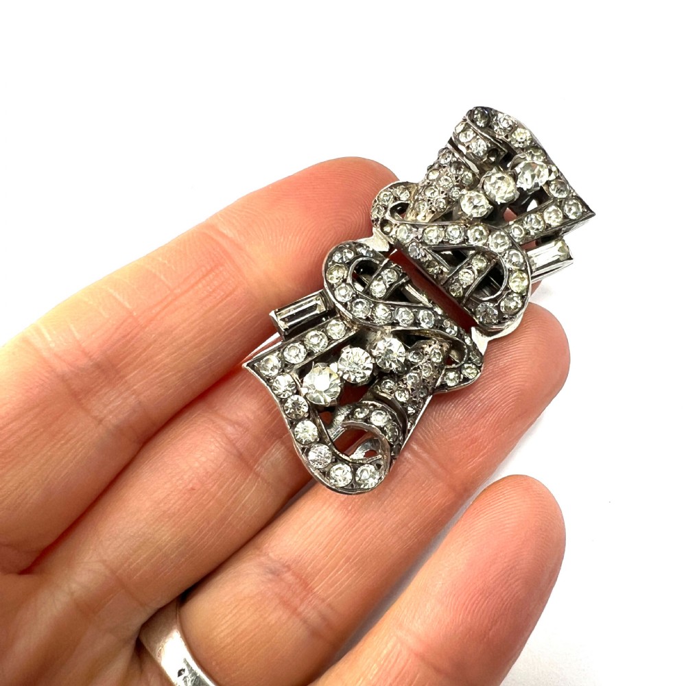 An Art Deco silver-tone paste duette brooch featuring geometric scrollwork set with round and baguette cut clear paste stones. View VII