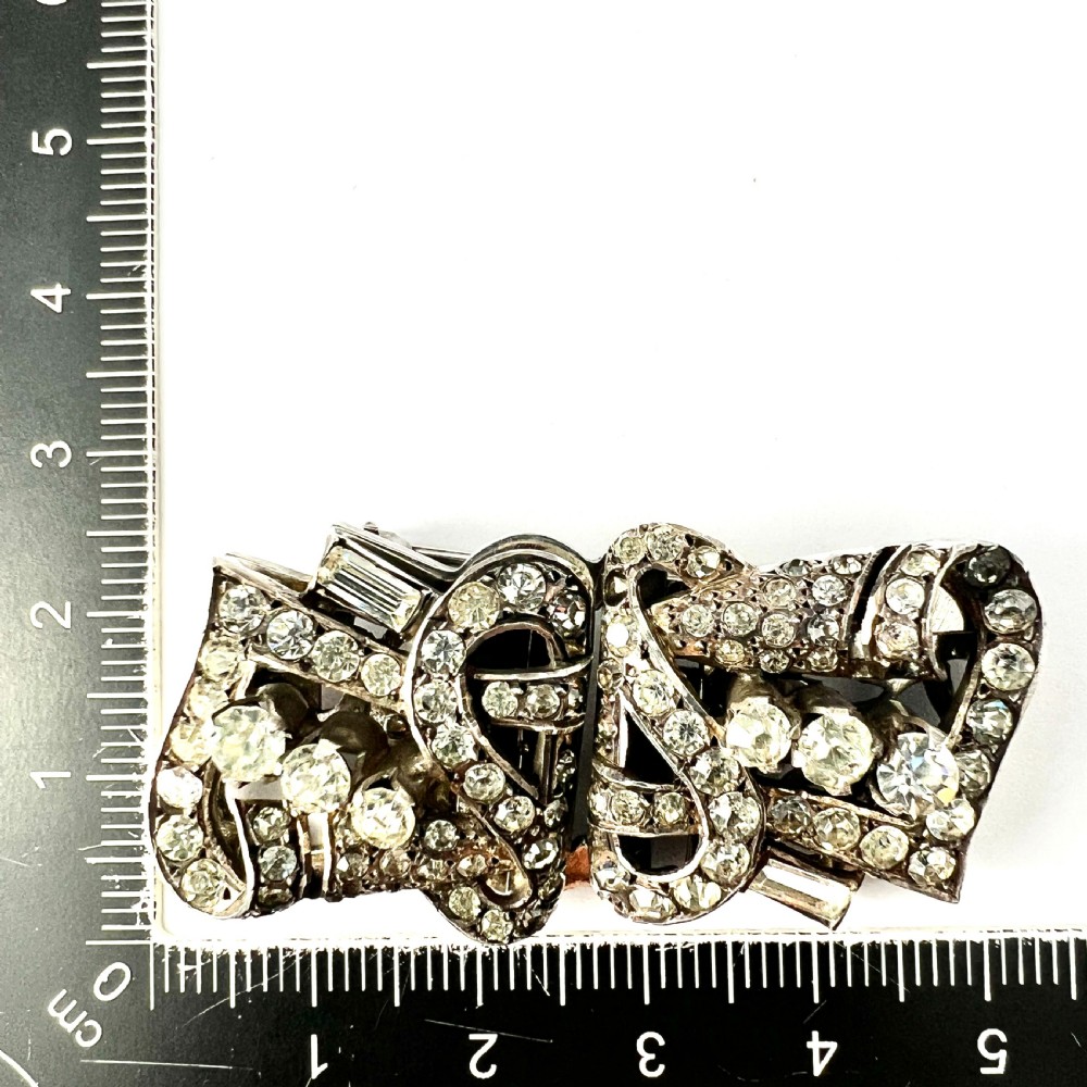 An Art Deco silver-tone paste duette brooch featuring geometric scrollwork set with round and baguette cut clear paste stones. View VIII
