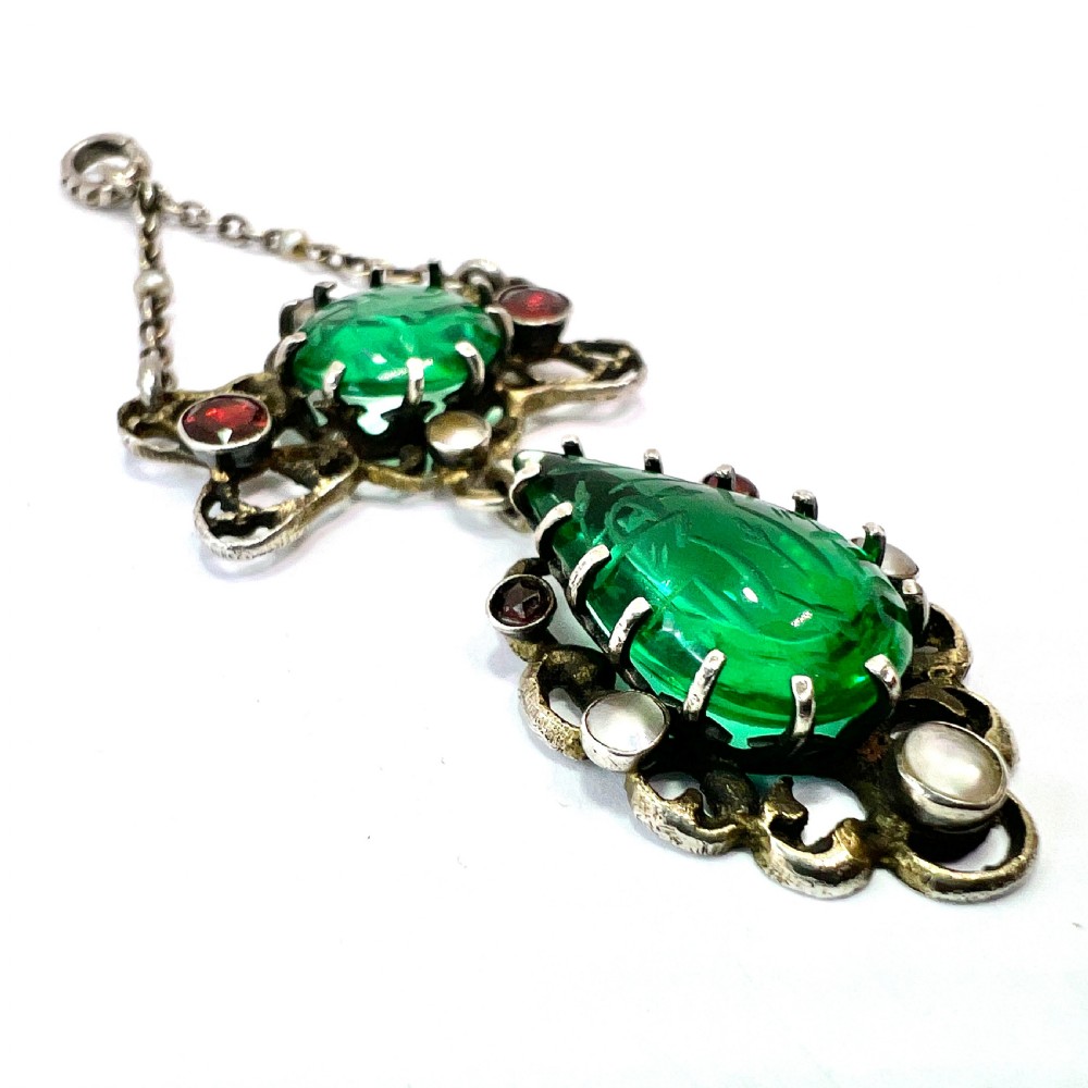 An antique silver pendant featuring carved green paste stones, round garnets, and seed pearls set in an openwork filigree frame. View III