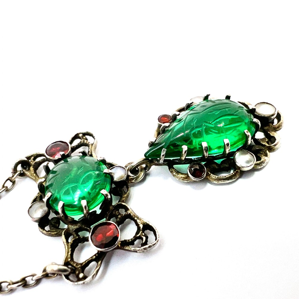 An antique silver pendant featuring carved green paste stones, round garnets, and seed pearls set in an openwork filigree frame. View V