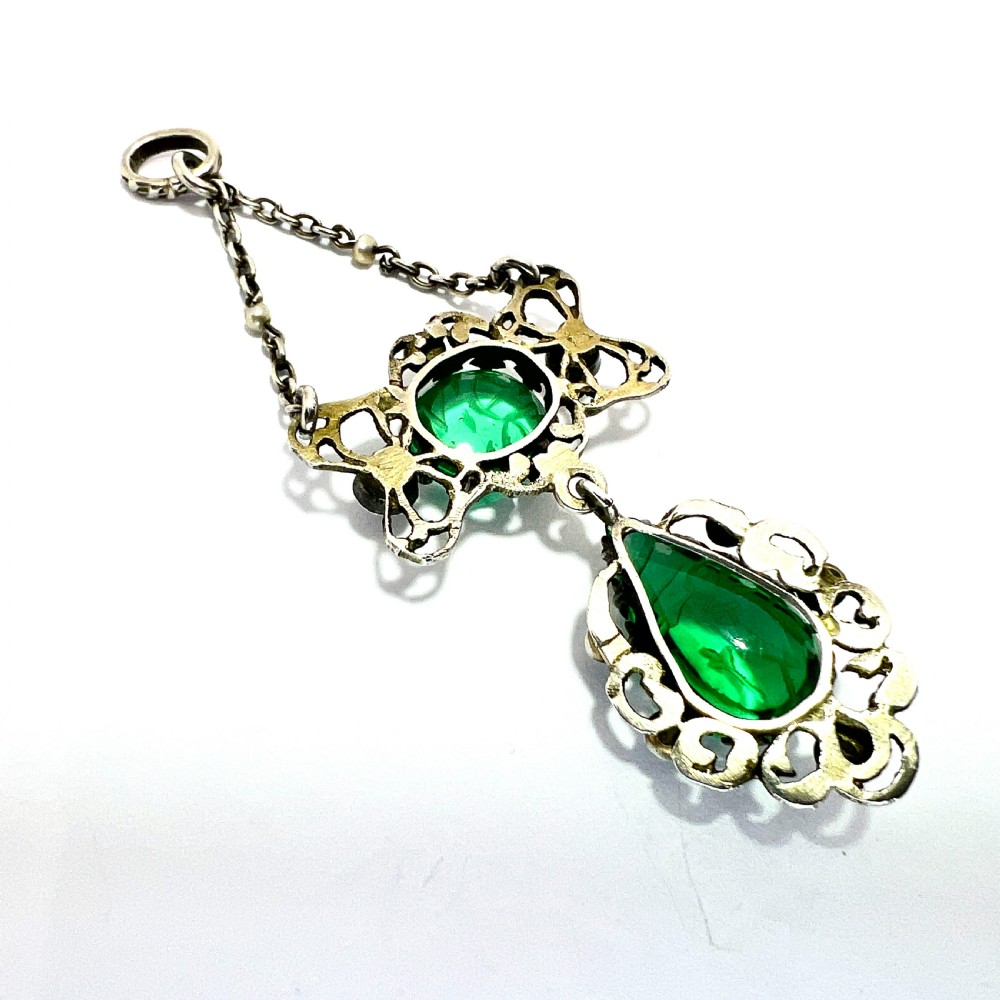 An antique silver pendant featuring carved green paste stones, round garnets, and seed pearls set in an openwork filigree frame. View VI