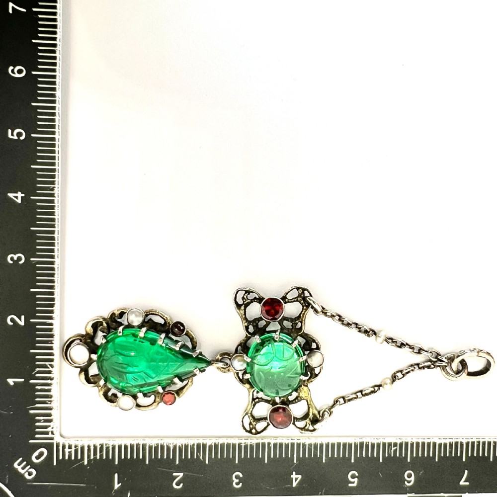 An antique silver pendant featuring carved green paste stones, round garnets, and seed pearls set in an openwork filigree frame. View VII