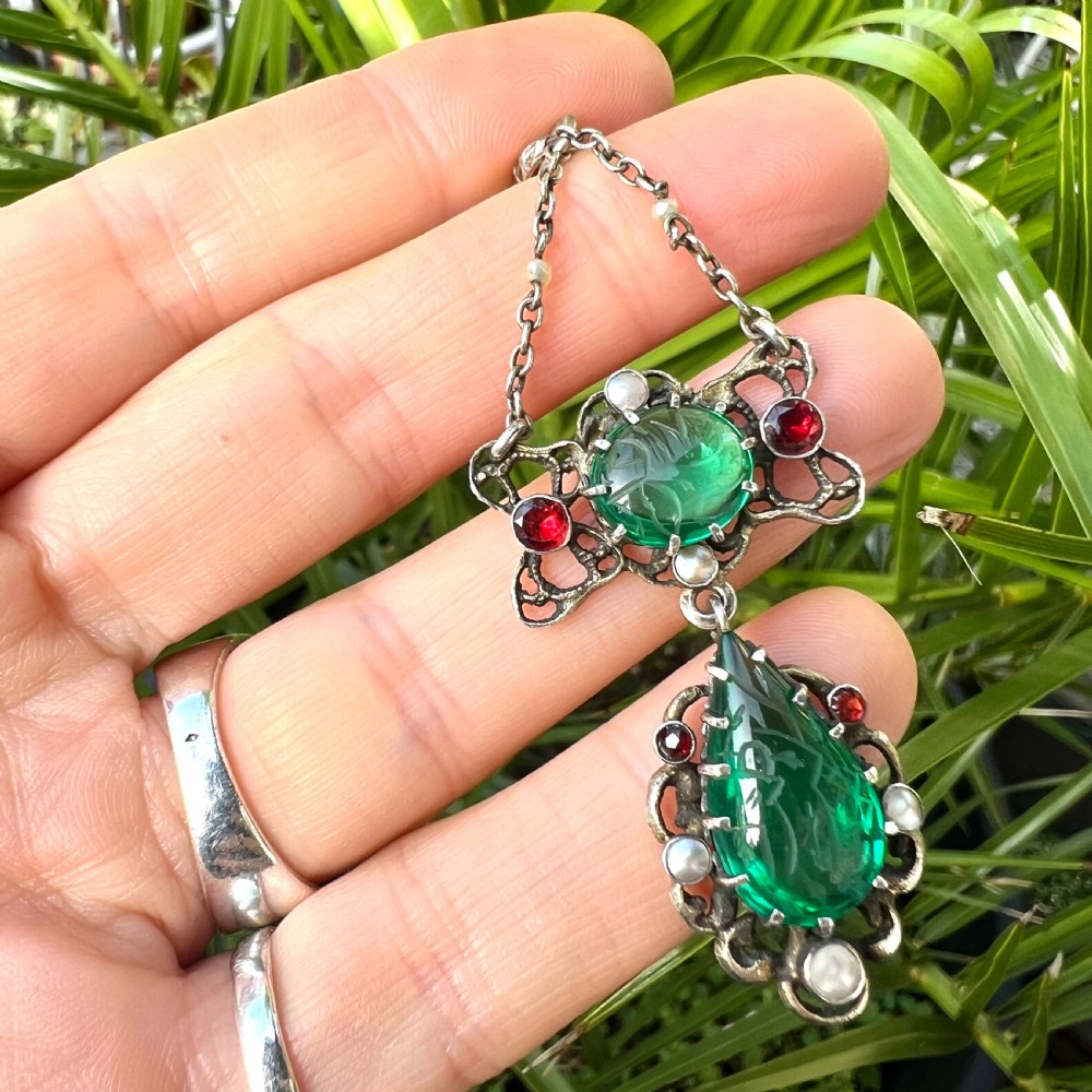 An antique silver pendant featuring carved green paste stones, round garnets, and seed pearls set in an openwork filigree frame. View VIII