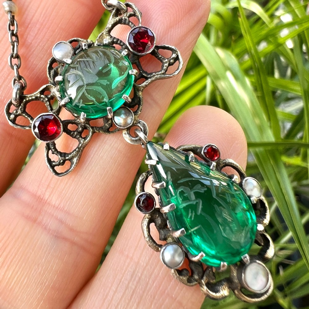 An antique silver pendant featuring carved green paste stones, round garnets, and seed pearls set in an openwork filigree frame. View IX
