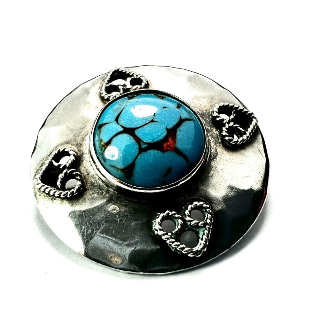 A circular hand-hammered silver brooch featuring a central turquoise glass cabochon framed by four rope-twist heart motifs.