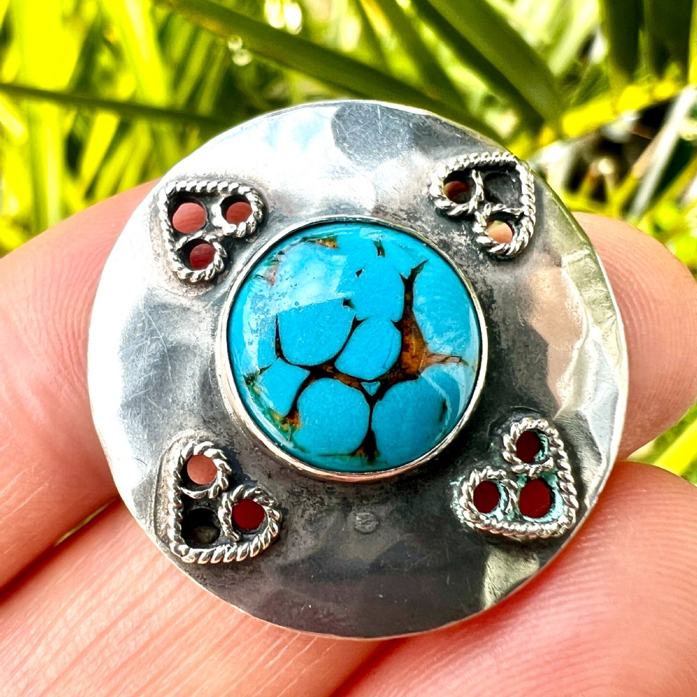 A circular hand-hammered silver brooch featuring a central turquoise glass cabochon framed by four rope-twist heart motifs. View VIII