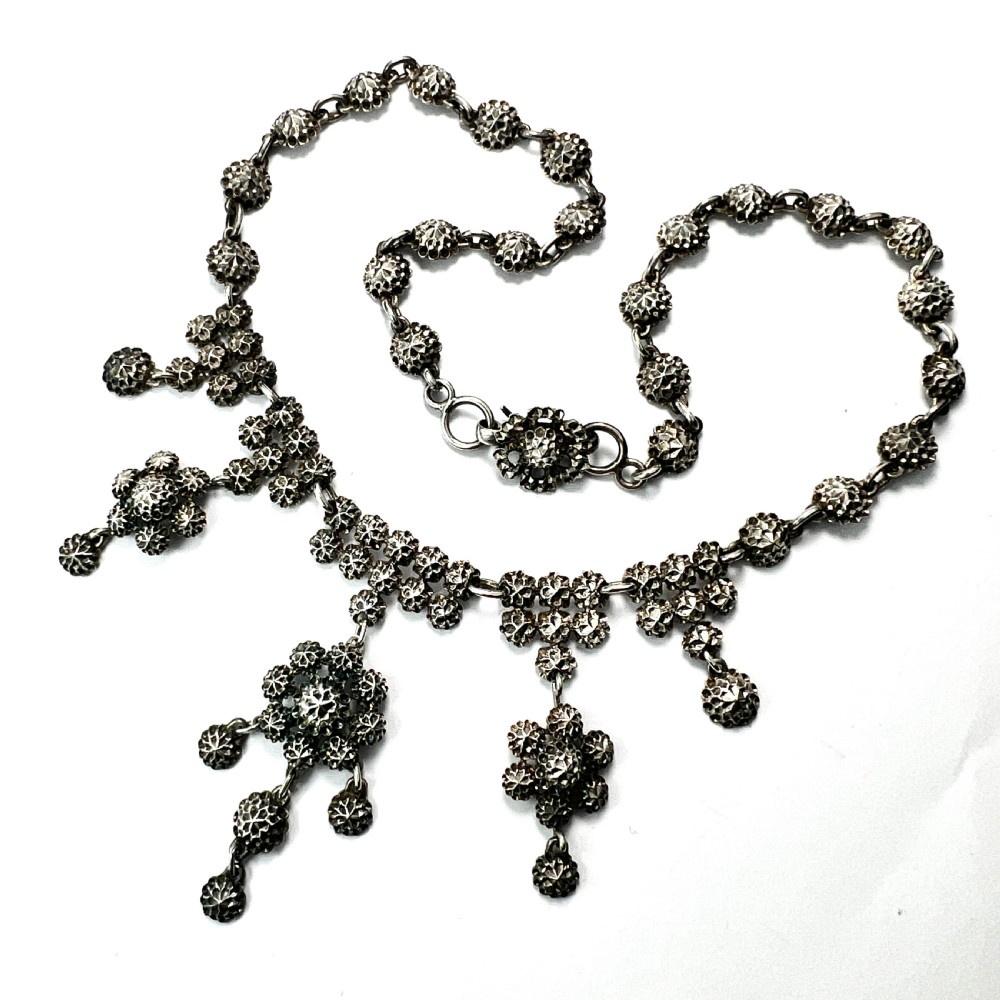 Victorian sterling silver necklace featuring textured spherical links and suspended chandelier drop motifs against a white backdrop.
