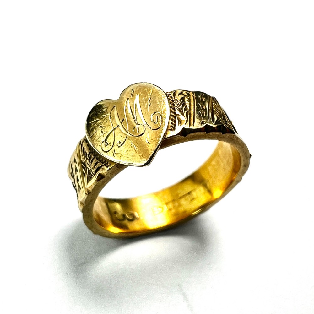 An Edwardian yellow gold ring featuring a central heart motif engraved with a monogram and shoulders decorated with chased scroll patterns.
