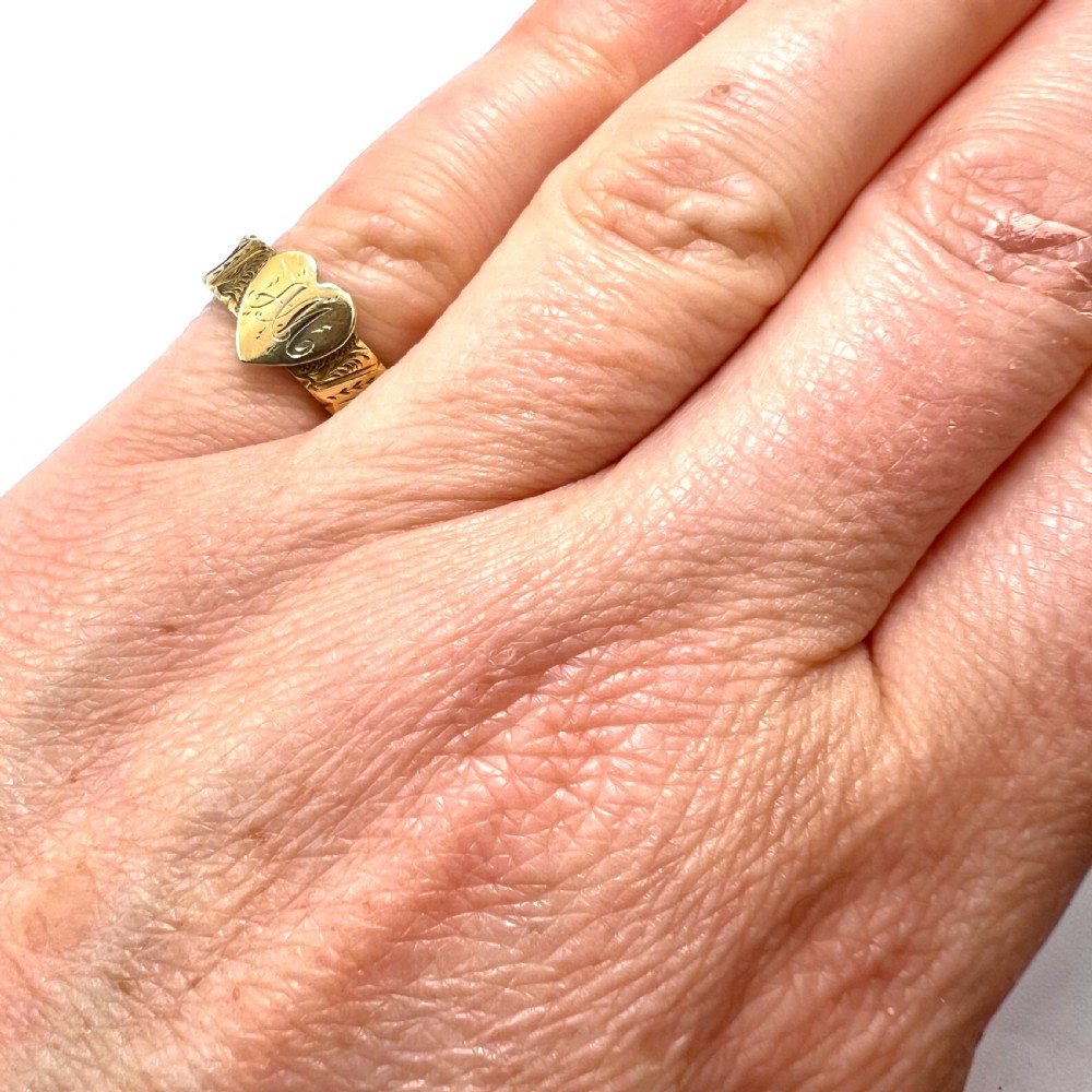 An Edwardian yellow gold ring featuring a central heart motif engraved with a monogram and shoulders decorated with chased scroll patterns. View VI