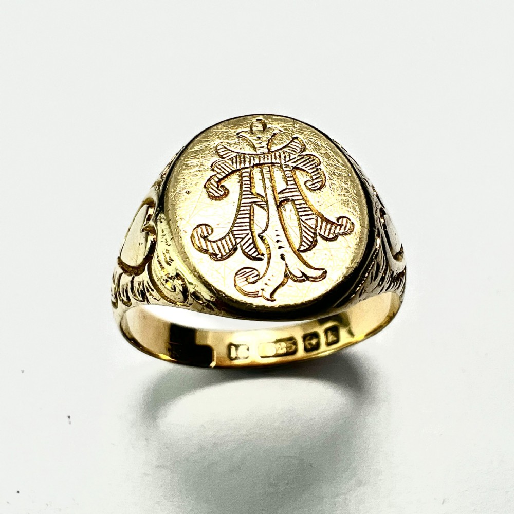 An antique yellow gold signet ring featuring an oval head with a hand-engraved monogram and detailed heart motifs on the shoulders.