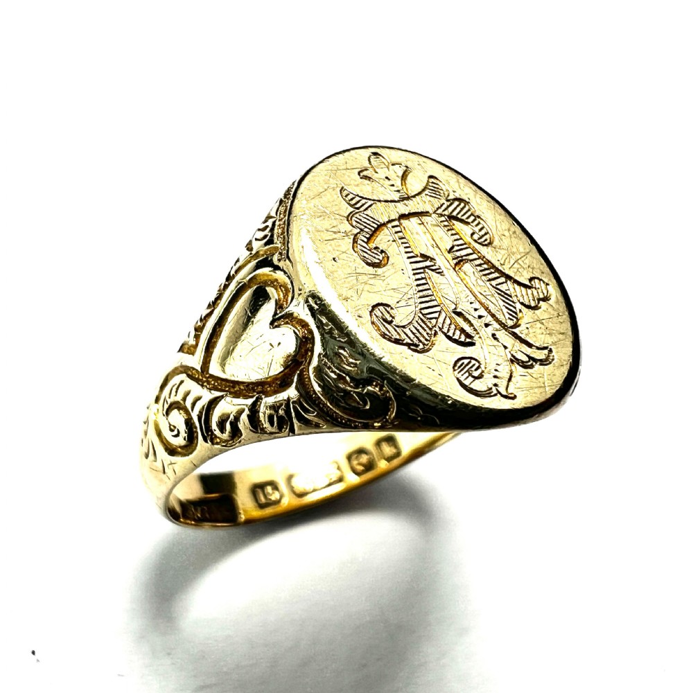 An antique yellow gold signet ring featuring an oval head with a hand-engraved monogram and detailed heart motifs on the shoulders. View II