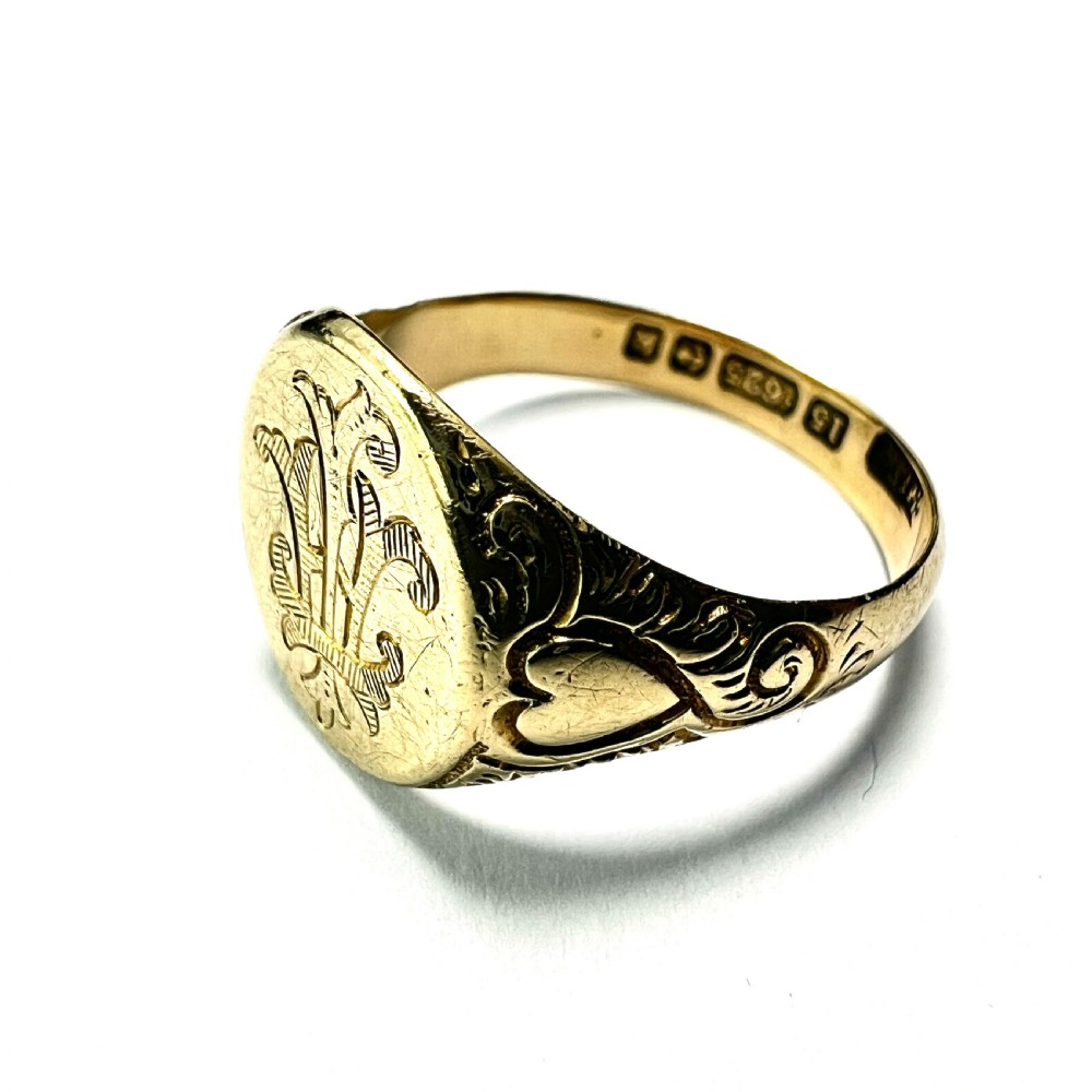 An antique yellow gold signet ring featuring an oval head with a hand-engraved monogram and detailed heart motifs on the shoulders. View V