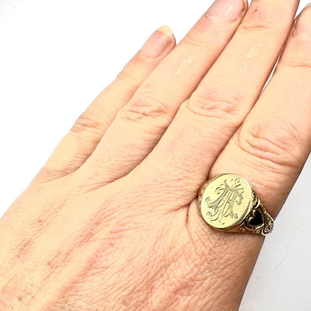 An antique yellow gold signet ring featuring an oval head with a hand-engraved monogram and detailed heart motifs on the shoulders. View VI