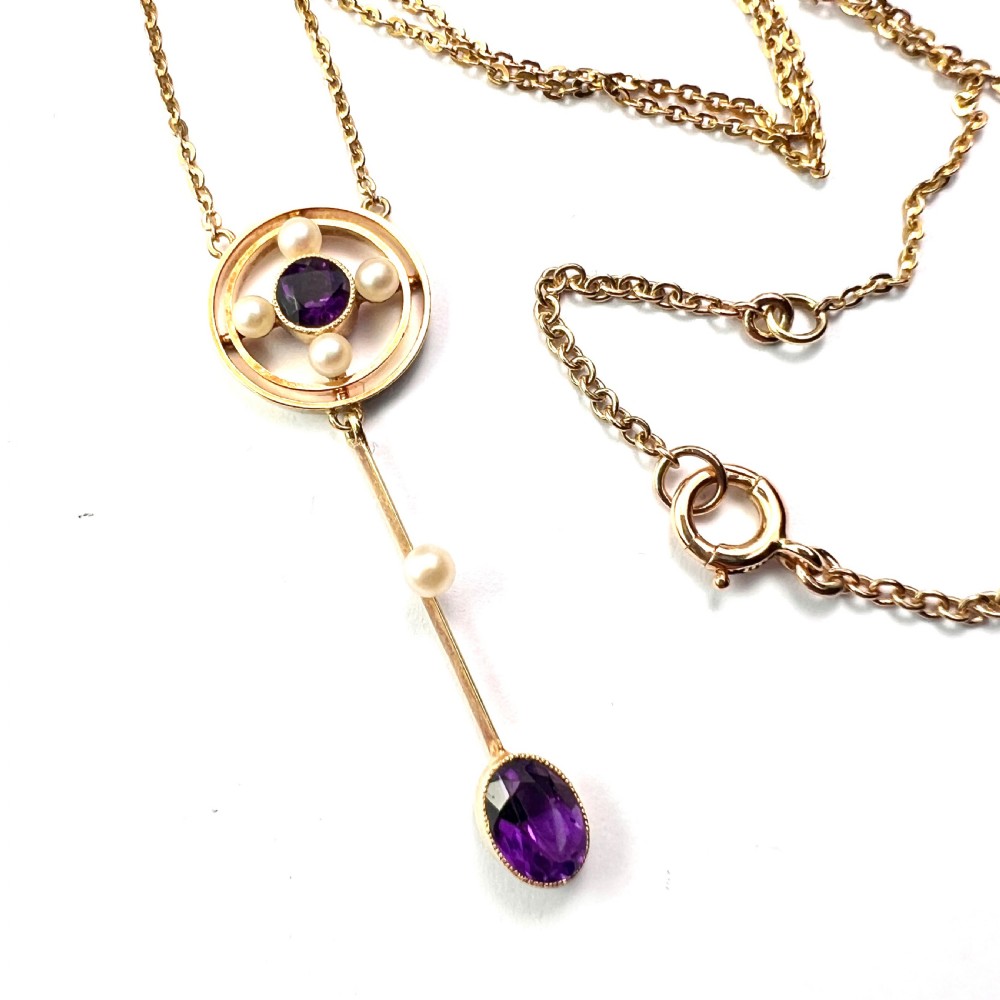 An Edwardian 15ct gold chain necklace featuring a circular pendant set with a round amethyst and four pearls, with a linear drop holding a seed pearl and an oval facet-cut amethyst.
