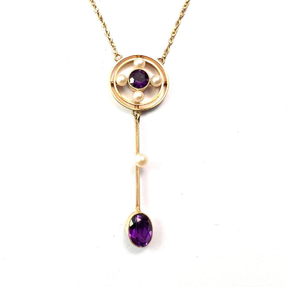 An Edwardian 15ct gold chain necklace featuring a circular pendant set with a round amethyst and four pearls, with a linear drop holding a seed pearl and an oval facet-cut amethyst. View II