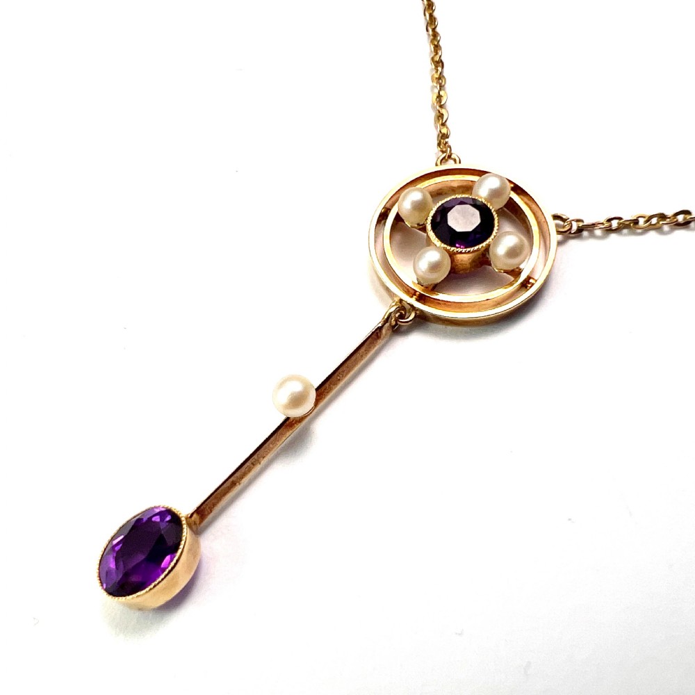 An Edwardian 15ct gold chain necklace featuring a circular pendant set with a round amethyst and four pearls, with a linear drop holding a seed pearl and an oval facet-cut amethyst. View III