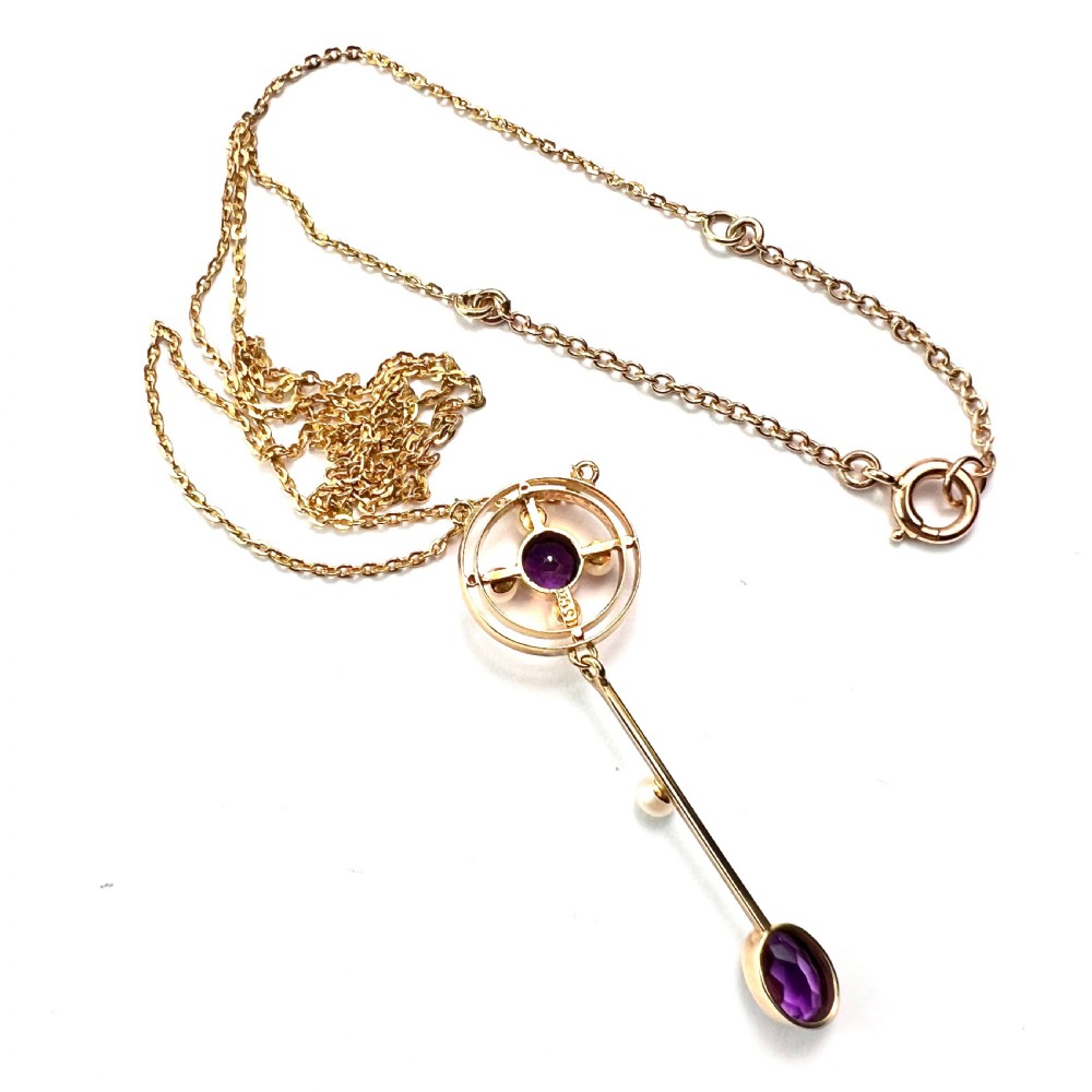 An Edwardian 15ct gold chain necklace featuring a circular pendant set with a round amethyst and four pearls, with a linear drop holding a seed pearl and an oval facet-cut amethyst. View V