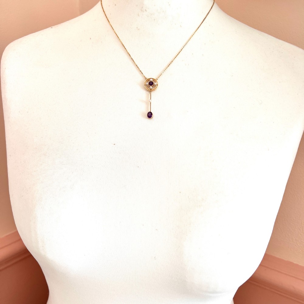 An Edwardian 15ct gold chain necklace featuring a circular pendant set with a round amethyst and four pearls, with a linear drop holding a seed pearl and an oval facet-cut amethyst. View VII