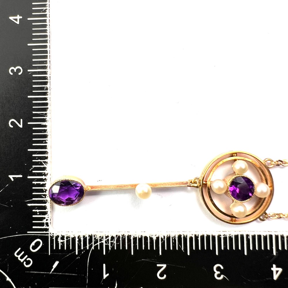 An Edwardian 15ct gold chain necklace featuring a circular pendant set with a round amethyst and four pearls, with a linear drop holding a seed pearl and an oval facet-cut amethyst. View IX