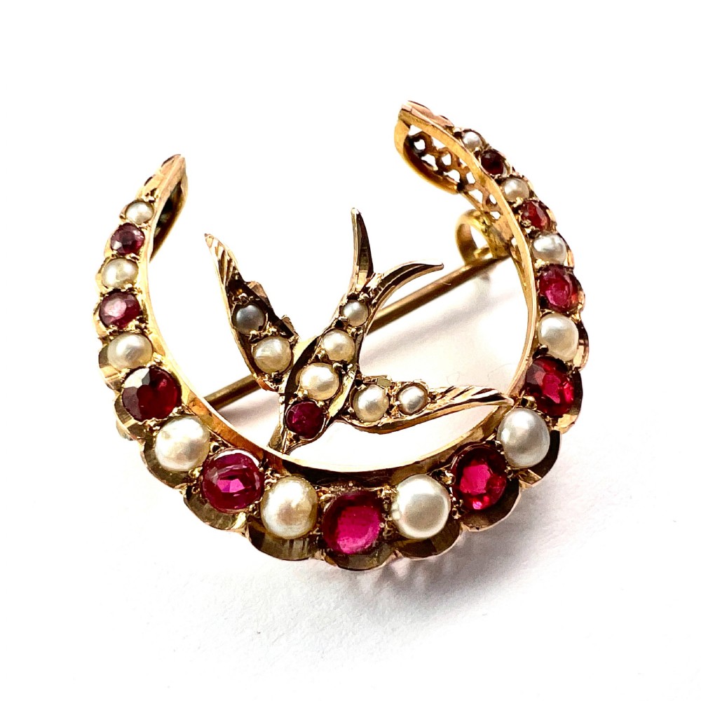 A 9ct gold crescent moon brooch set with alternating rubies and seed pearls surrounding a central swallow motif embellished with pearls and a ruby eye. View II