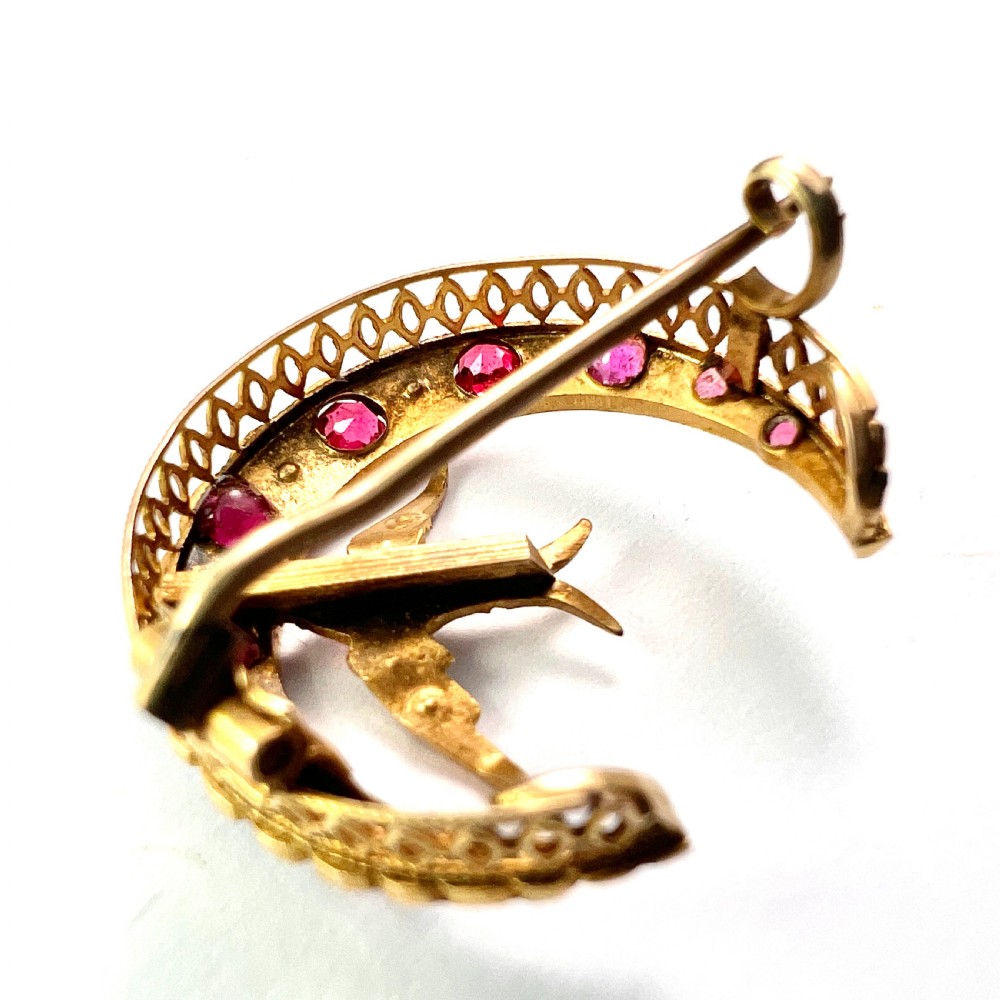 A 9ct gold crescent moon brooch set with alternating rubies and seed pearls surrounding a central swallow motif embellished with pearls and a ruby eye. View V