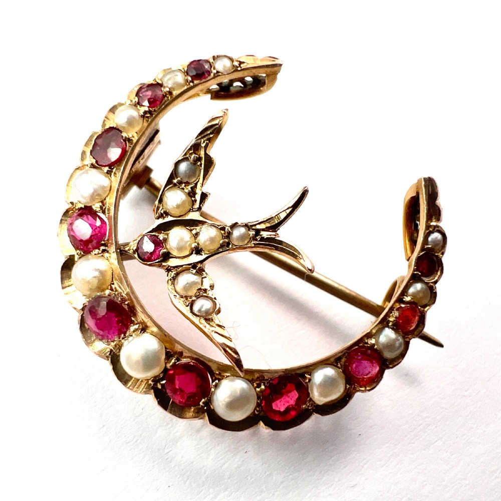 A 9ct gold crescent moon brooch set with alternating rubies and seed pearls surrounding a central swallow motif embellished with pearls and a ruby eye. View VI